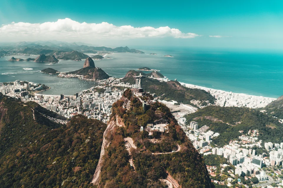 Aerial view of a rocky green summit above a dense coastal city, sandy beaches and turquoise ocean