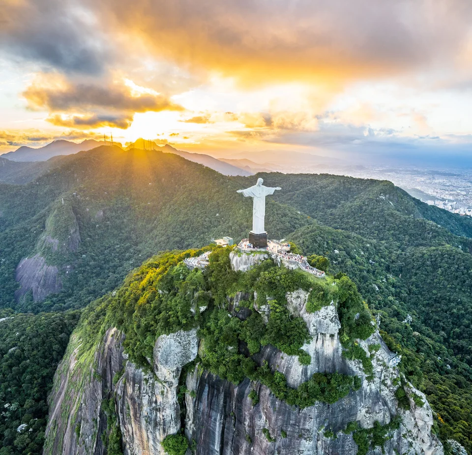 Christ the Redeemer standing on a steep forested summit beneath clouds lit by the setting sun