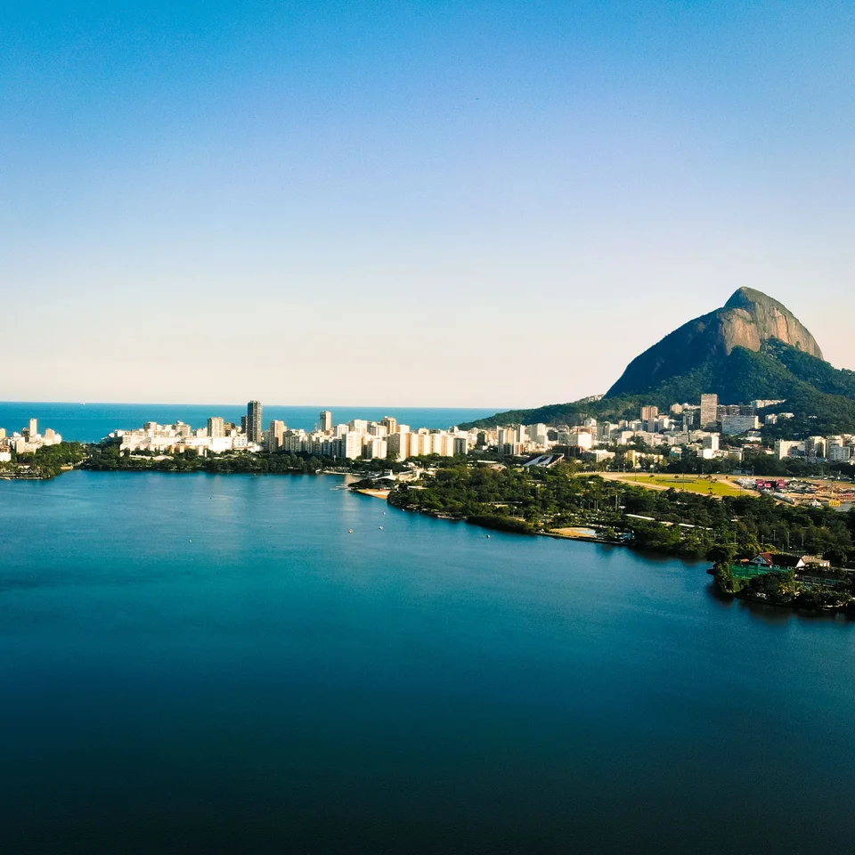 Calm blue lagoon bordered by green trees and city buildings with a steep mountain in the distance