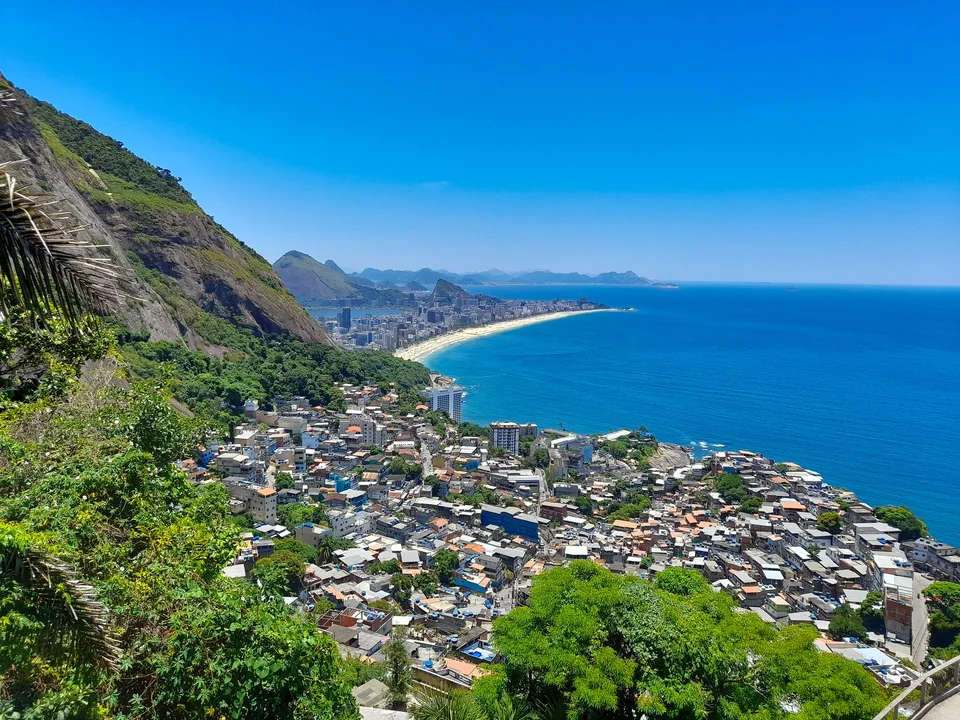 Colorful buildings covering a green hillside above a wide blue ocean and curving distant beach