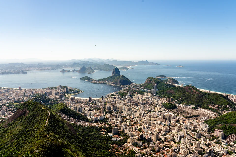 Wide view of dense city streets, green mountain ridges and rounded rocky peaks beside a blue bay
