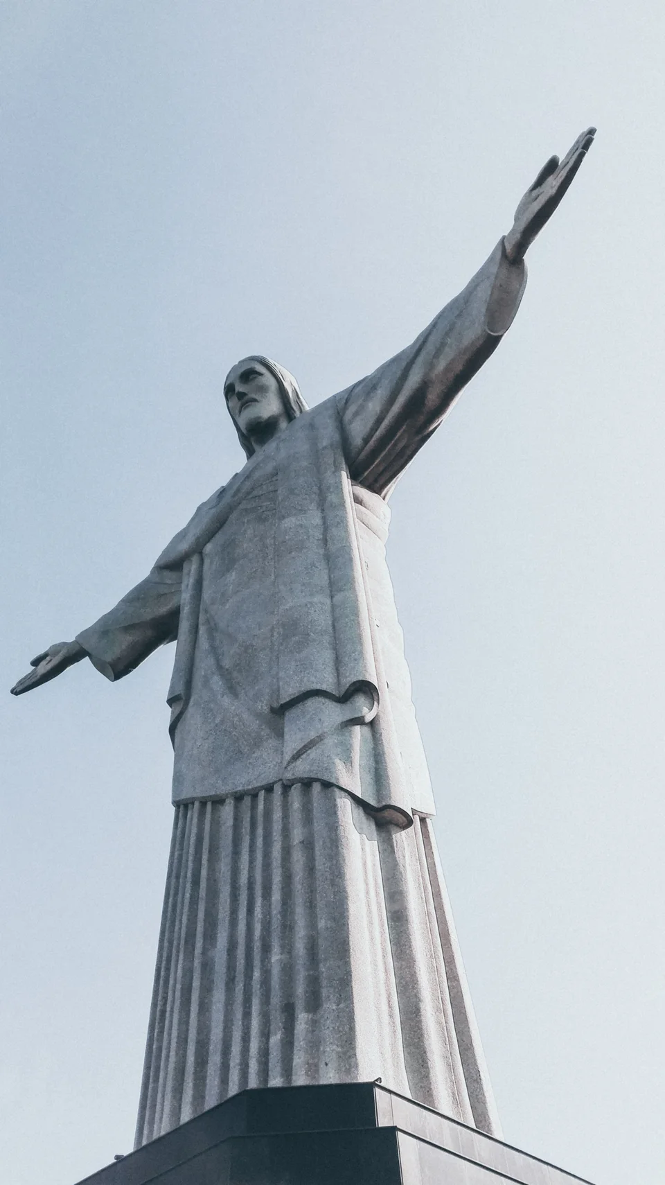 Low-angle view of Christ the Redeemer with outstretched arms against a pale cloudy sky