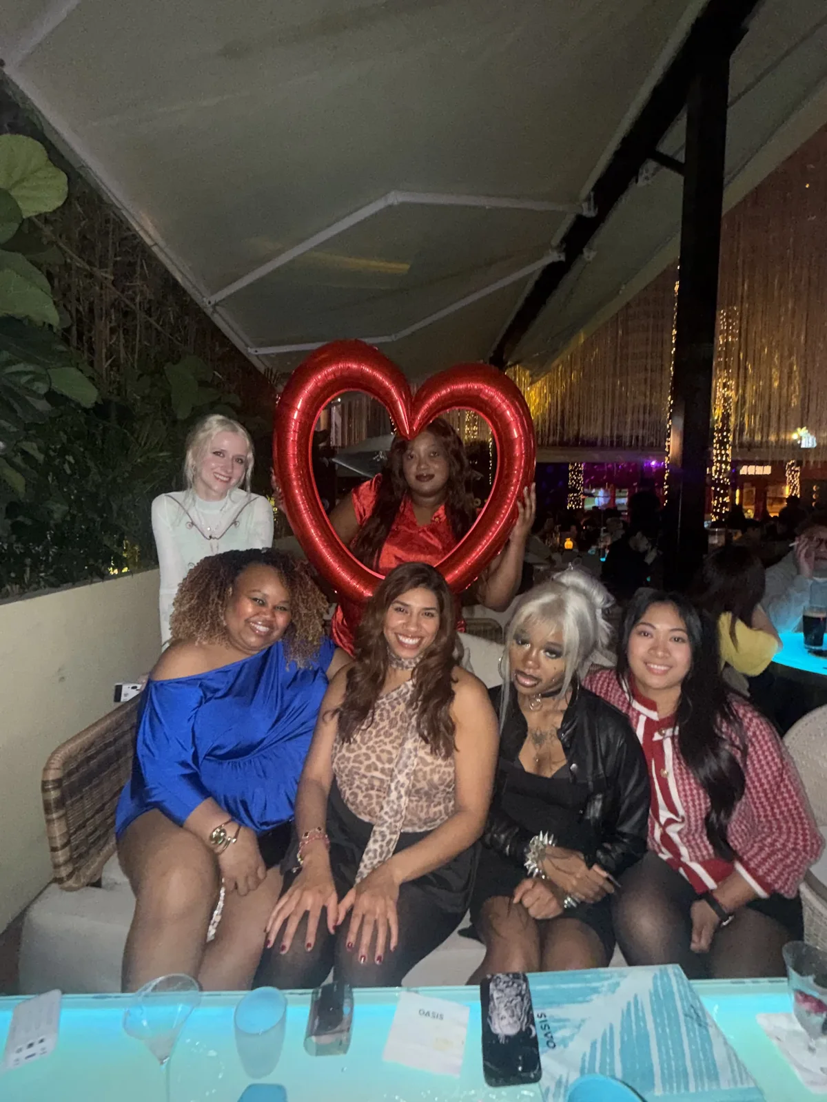 Friends gathered around a dinner table with a red heart decoration behind them