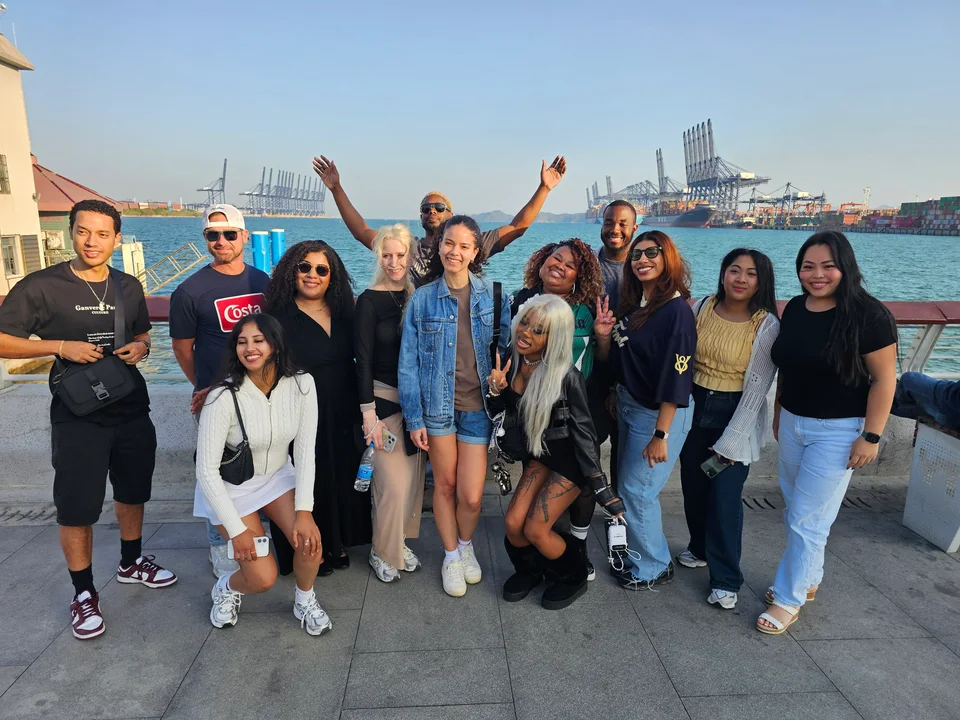 The group smiling together on a waterfront promenade with a city skyline across the water