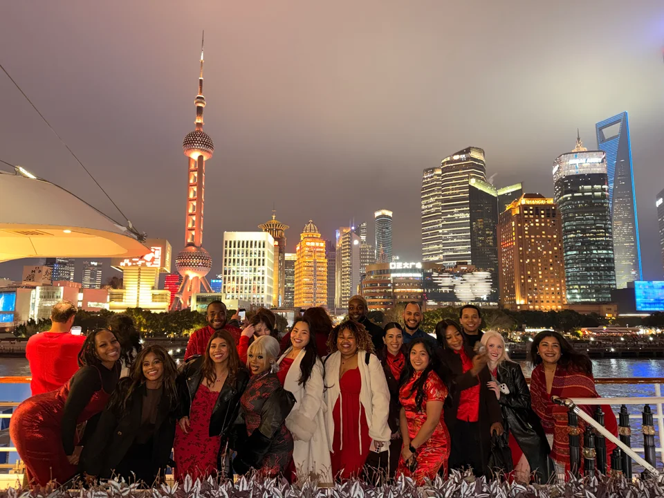 The group gathered at a railing with Shanghai towers glowing across the water
