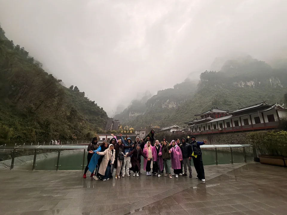 Travelers gathered beside a pool and low buildings beneath mist-covered mountains