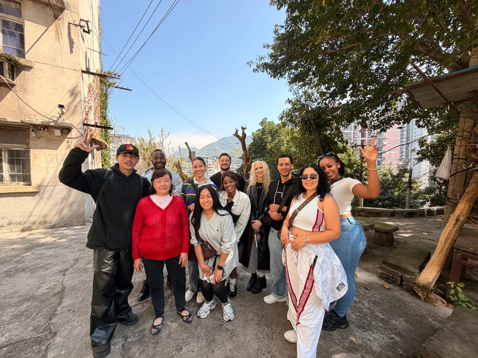 The group smiling in a sunny neighborhood lane lined with buildings and trees